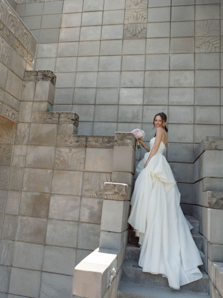 Bride posing in strapless gown against modern architectural stone wall