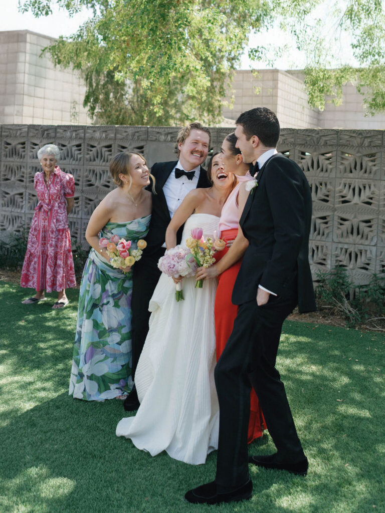Bride and groom smiling with bridal party holding colorful bouquets