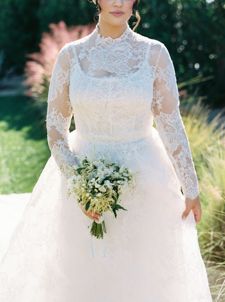 Bride holding bouquet in lace gown in Arizona desert.