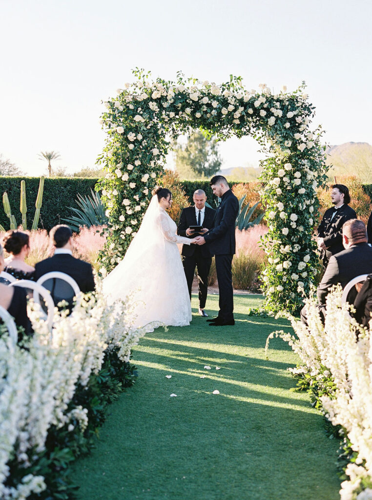 Bride and groom exchanging vows under lush floral arch in Scottsdale.