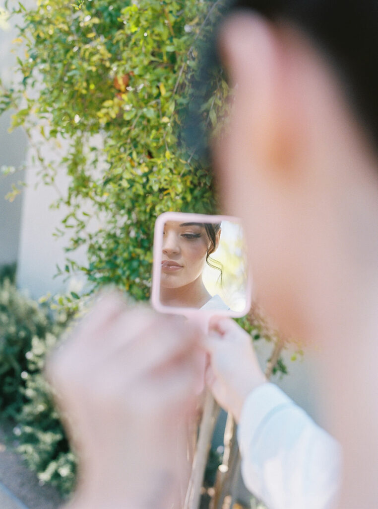 Bride touching up lipstick in mirror before wedding ceremony.