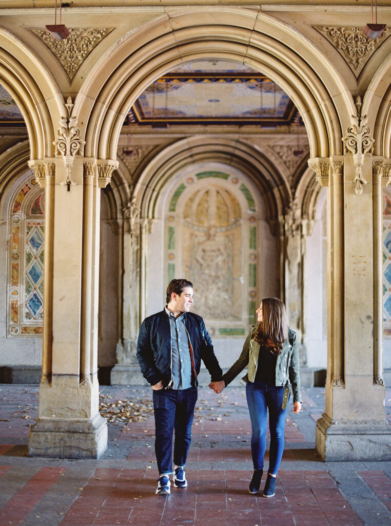 Couple walking hand-in-hand under Bethesda Terrace during NYC fall engagement session