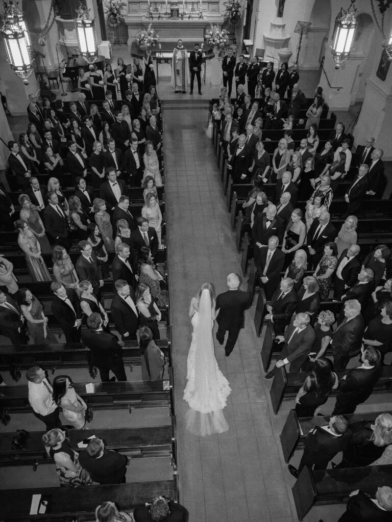 Bride walking down the aisle at Brophy Chapel with guests seated.