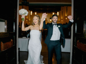 Bride and groom exit with joy, raising arms in celebration.