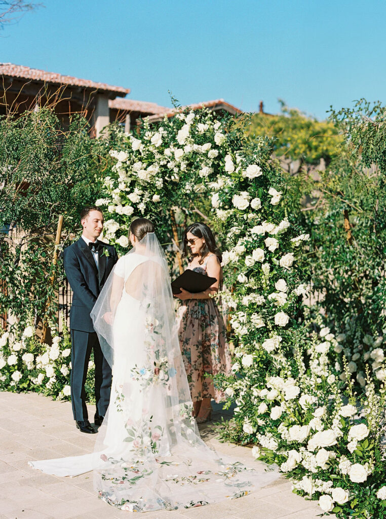 Bride and groom standing with officiant under floral arch