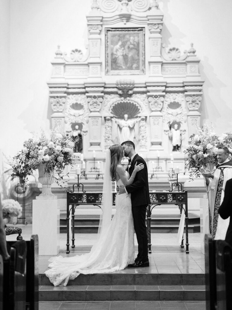 Bride and groom kiss at altar inside Brophy Chapel.