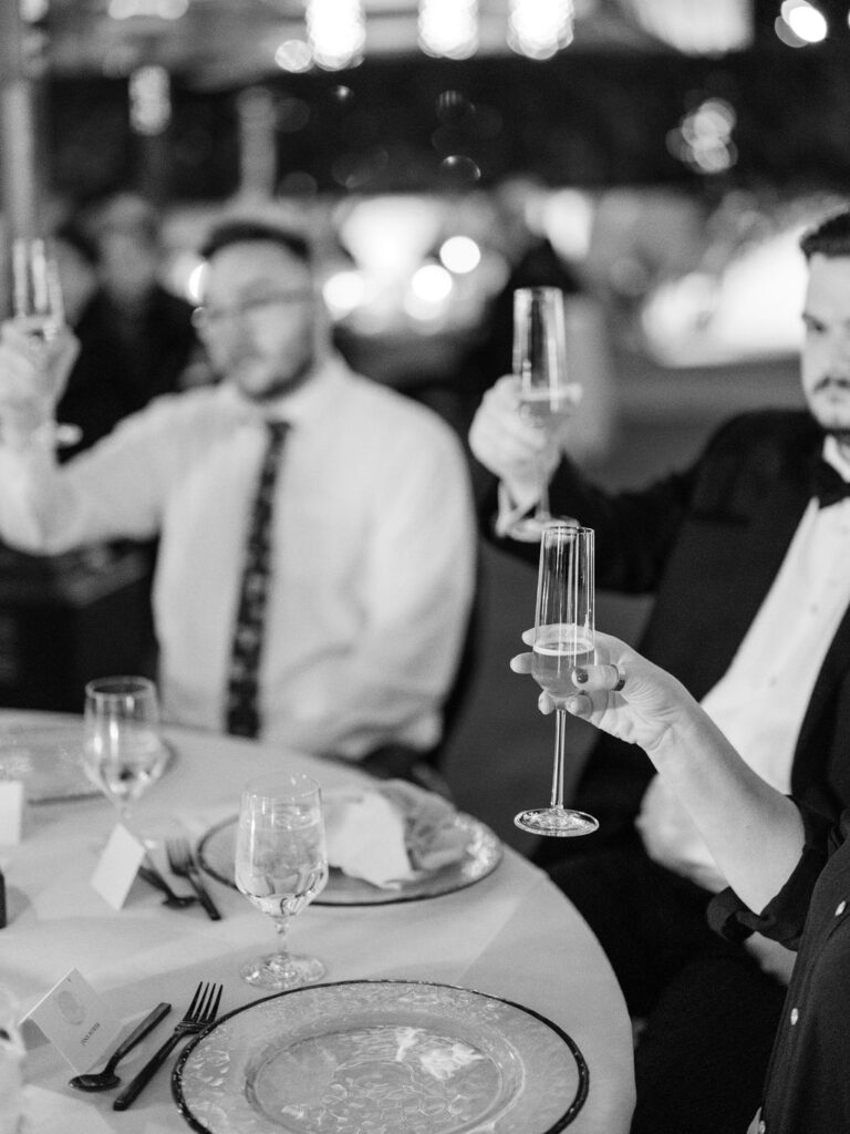 Guests raising champagne glasses in black and white wedding photo.