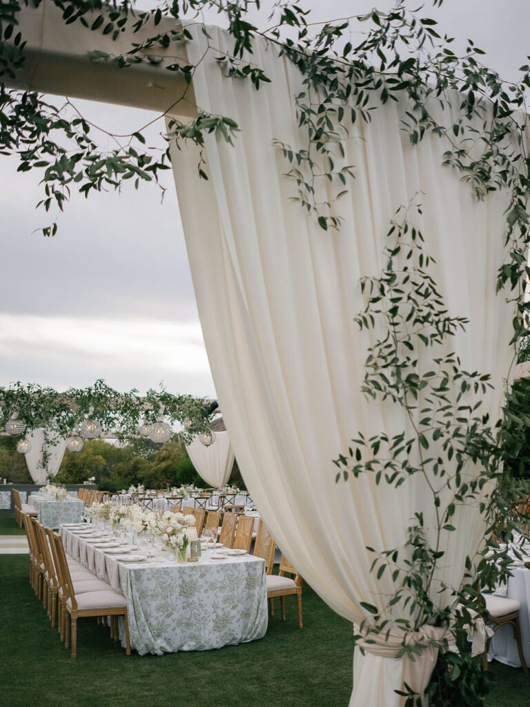 Outdoor wedding reception table with draping and greenery.