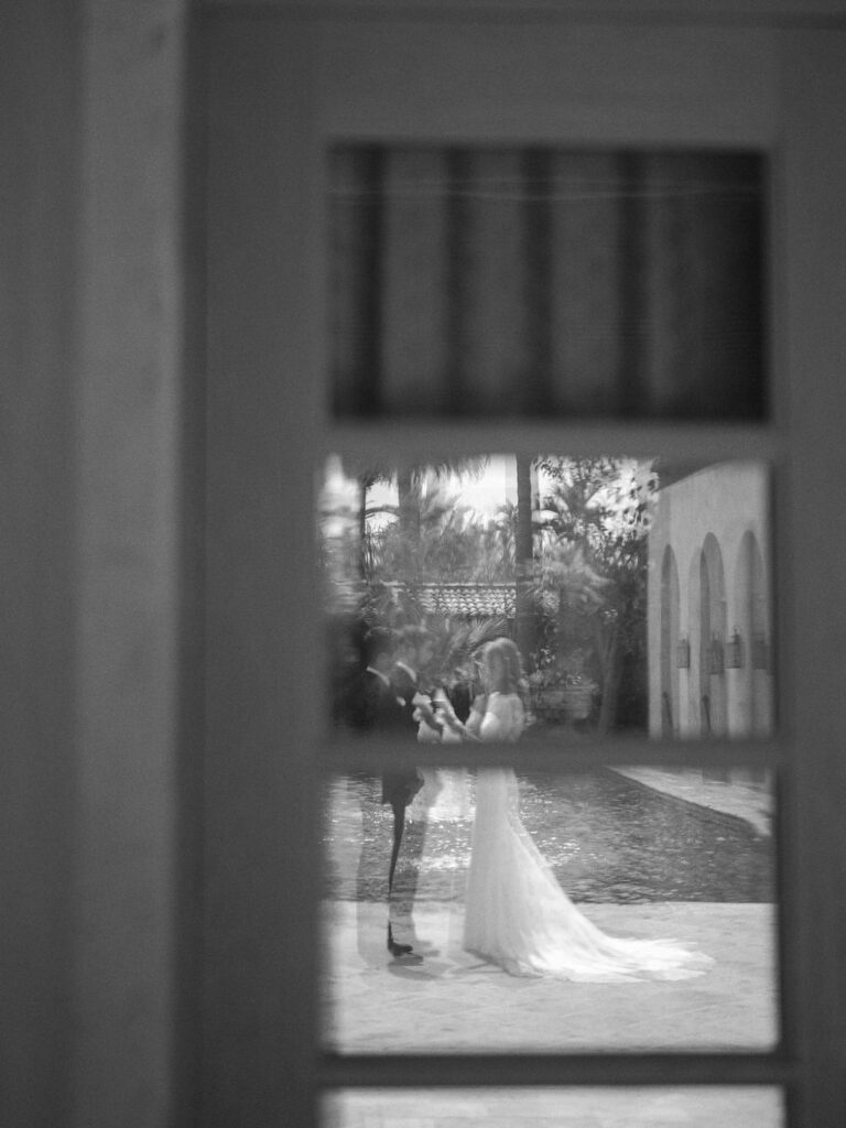 Bride and groom framed through window reflection.