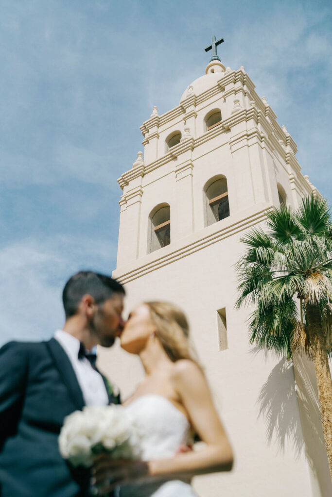 Bride and groom kiss outside Brophy Chapel under white tower.