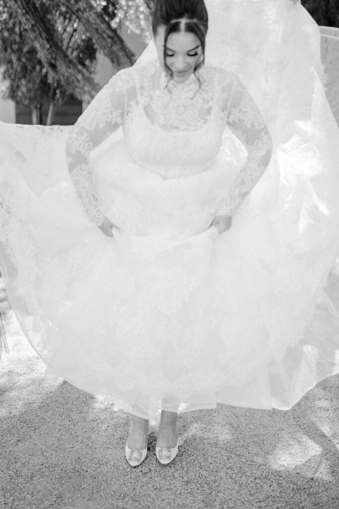 Bride holding lace gown detail outdoors in natural light.