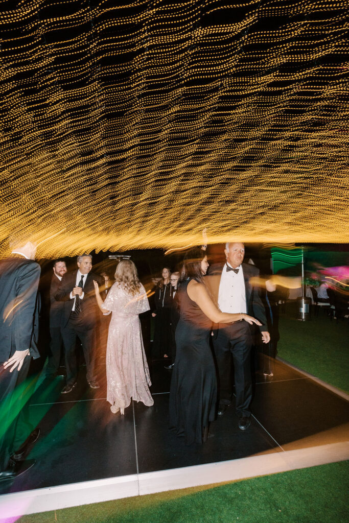 Wedding guests dancing under golden lights during reception.