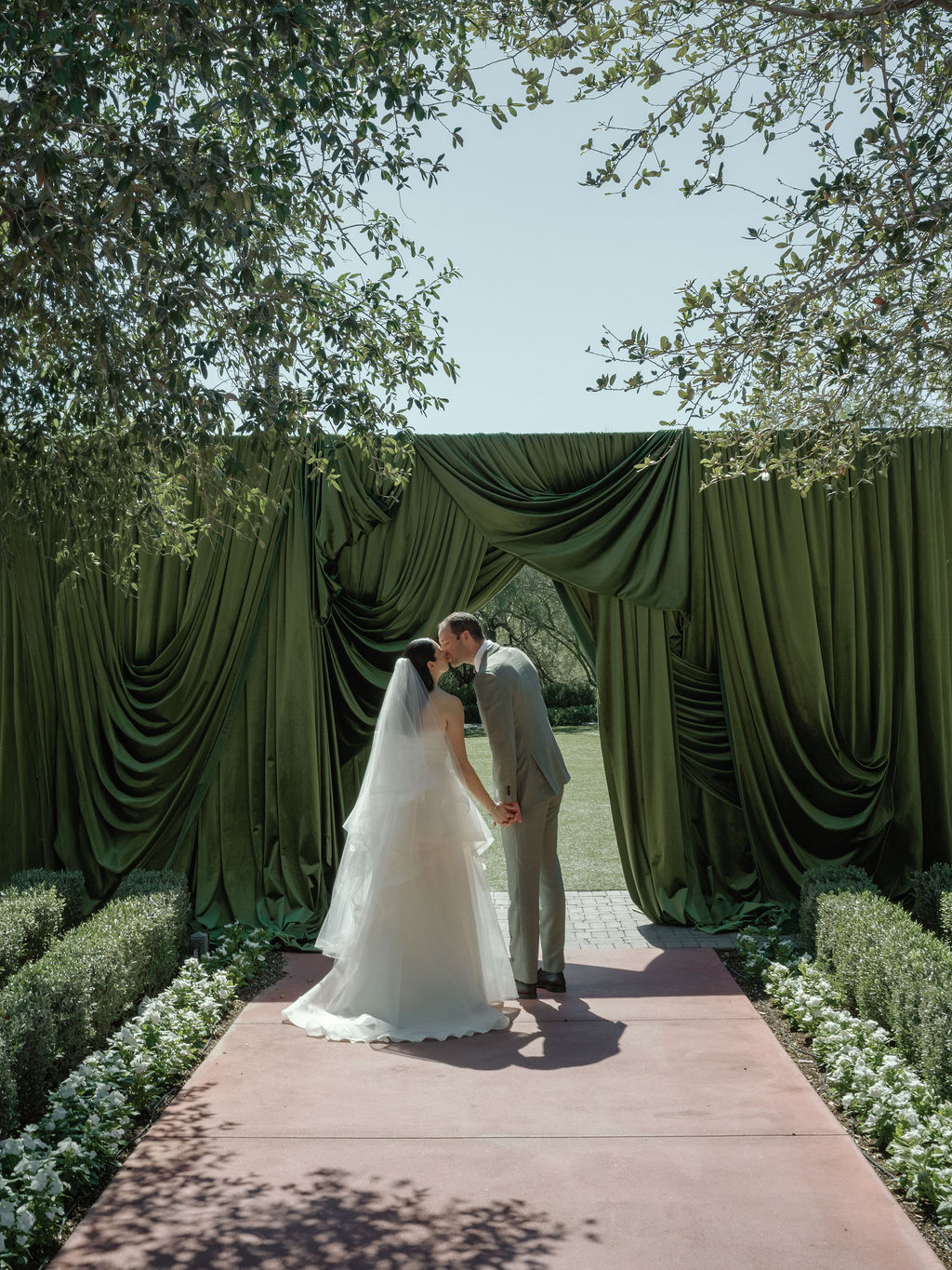 Newlyweds kissing under a green draped arch after their ceremony