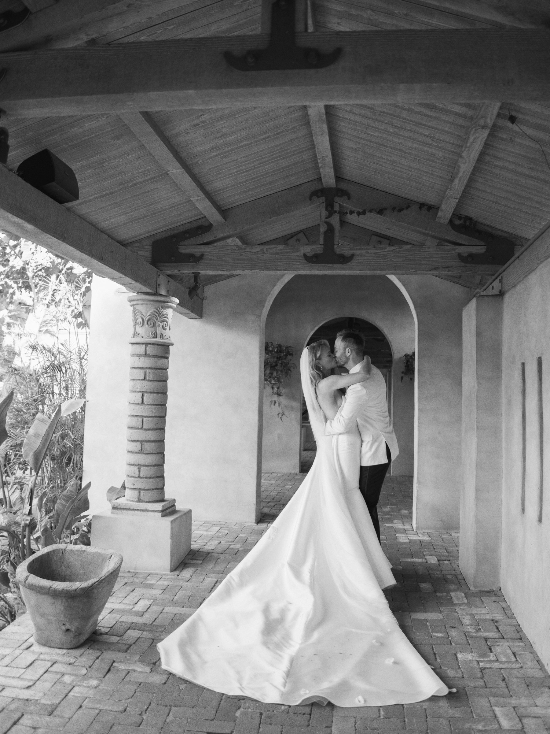 Black-and-white portrait of Meg and Peter kissing beneath a shaded arch