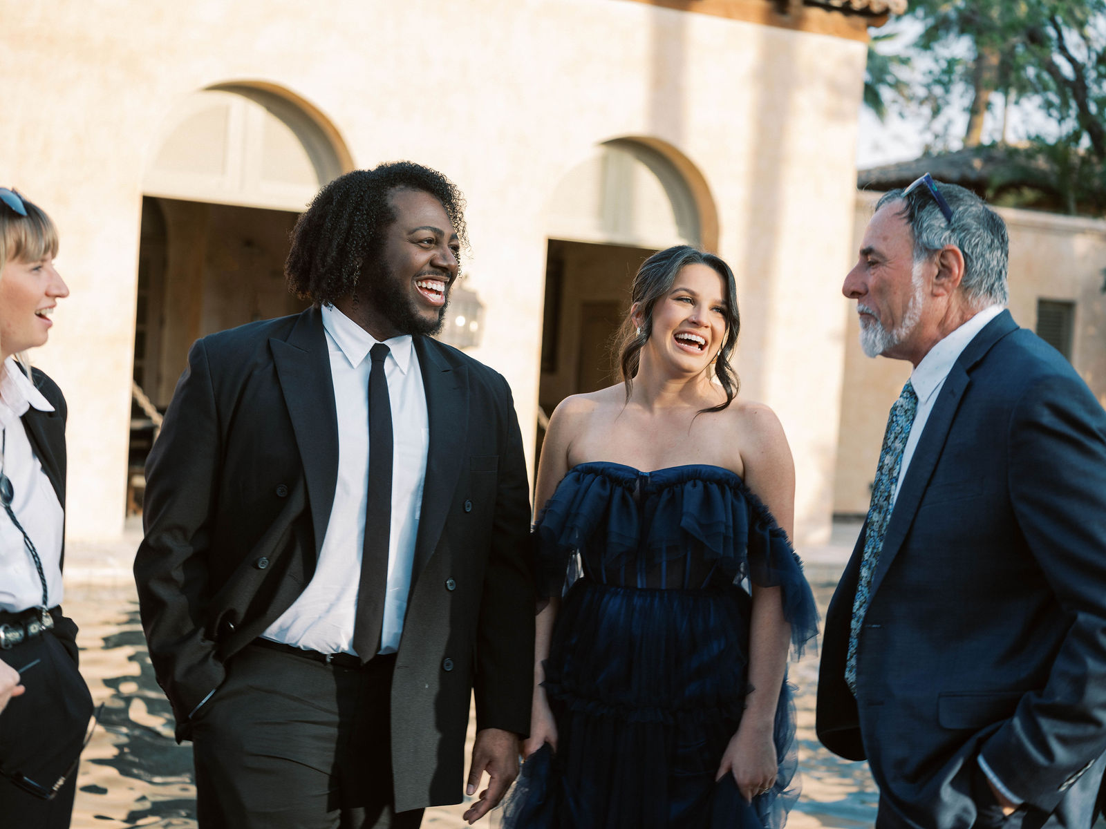 Wedding guests laugh together beside the Royal Palms arches