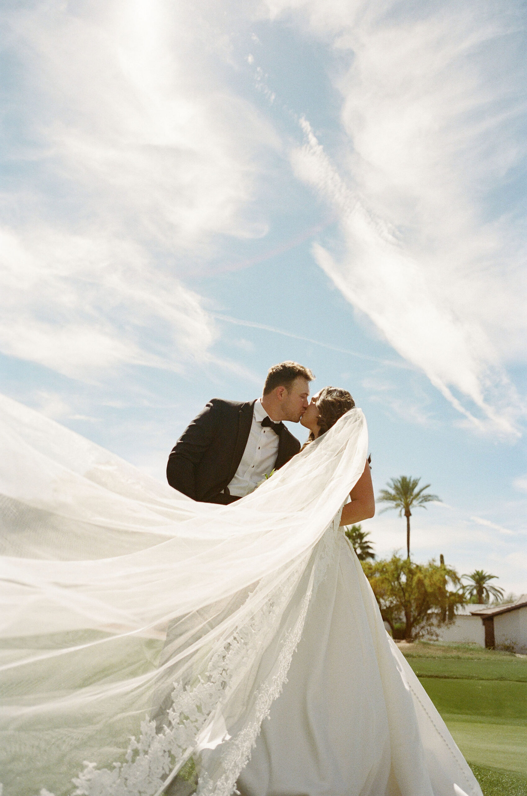 Taylor and Ryan kissing beneath a sweeping veil and cloud-filled sky on film.