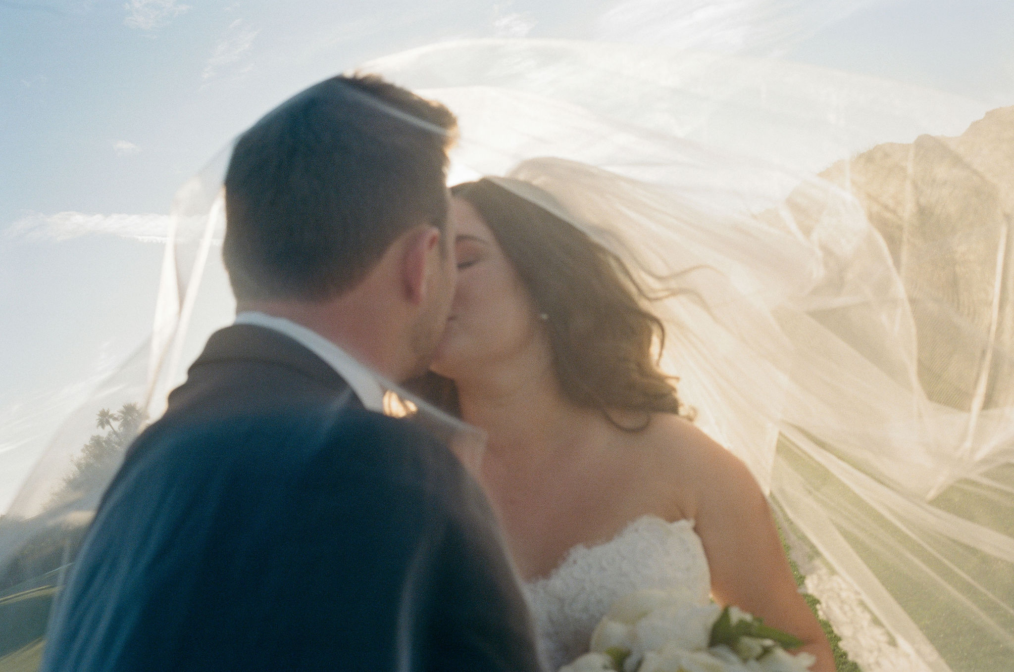 A sunlit close kiss with the veil floating around Taylor and Ryan, photographed on film.