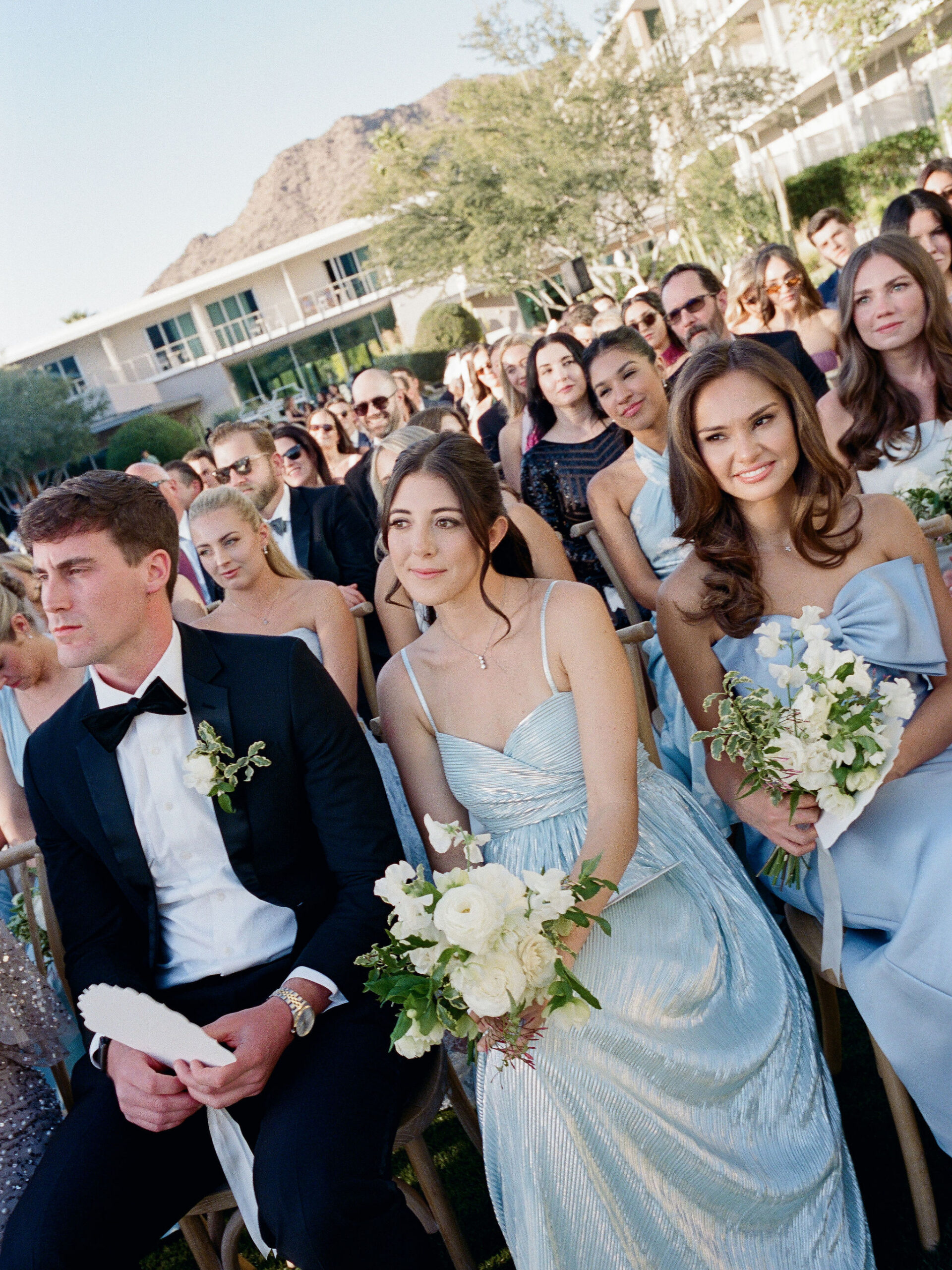Wedding guests in pale blue framed closely during the ceremony on film.