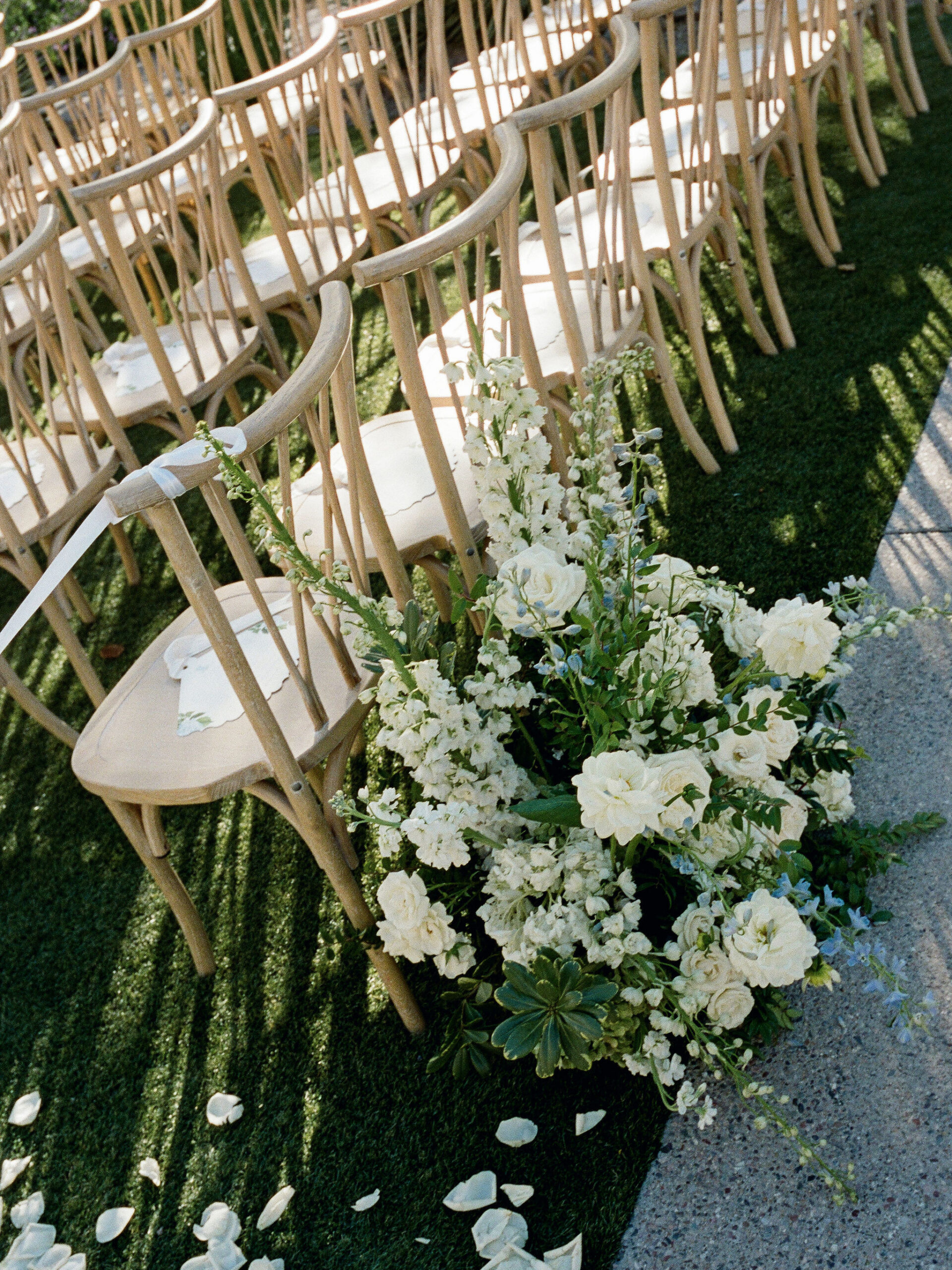 White flowers and rows of wooden ceremony chairs in sunlight on film.