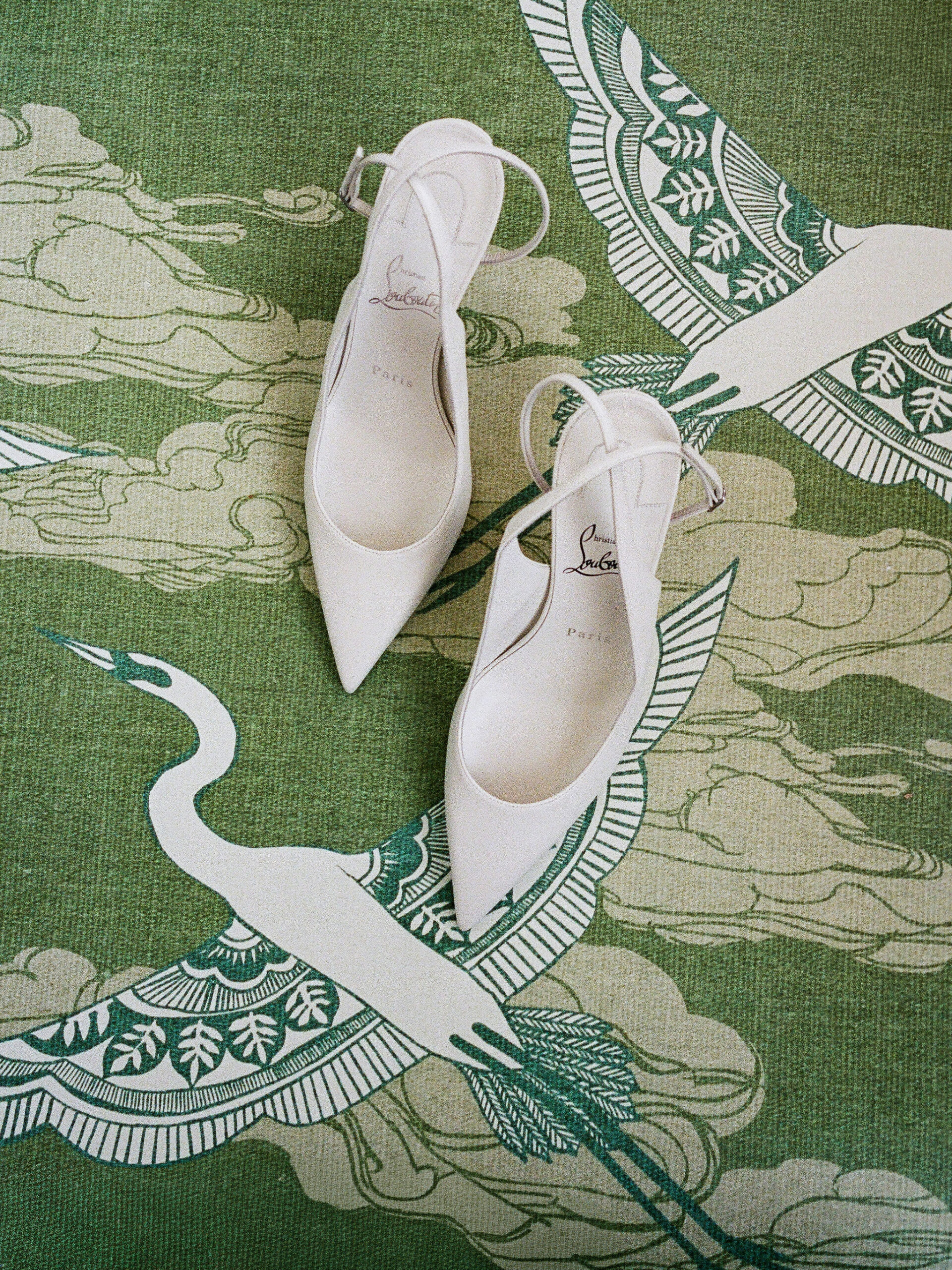 White bridal shoes on green fabric patterned with cranes, photographed on film.