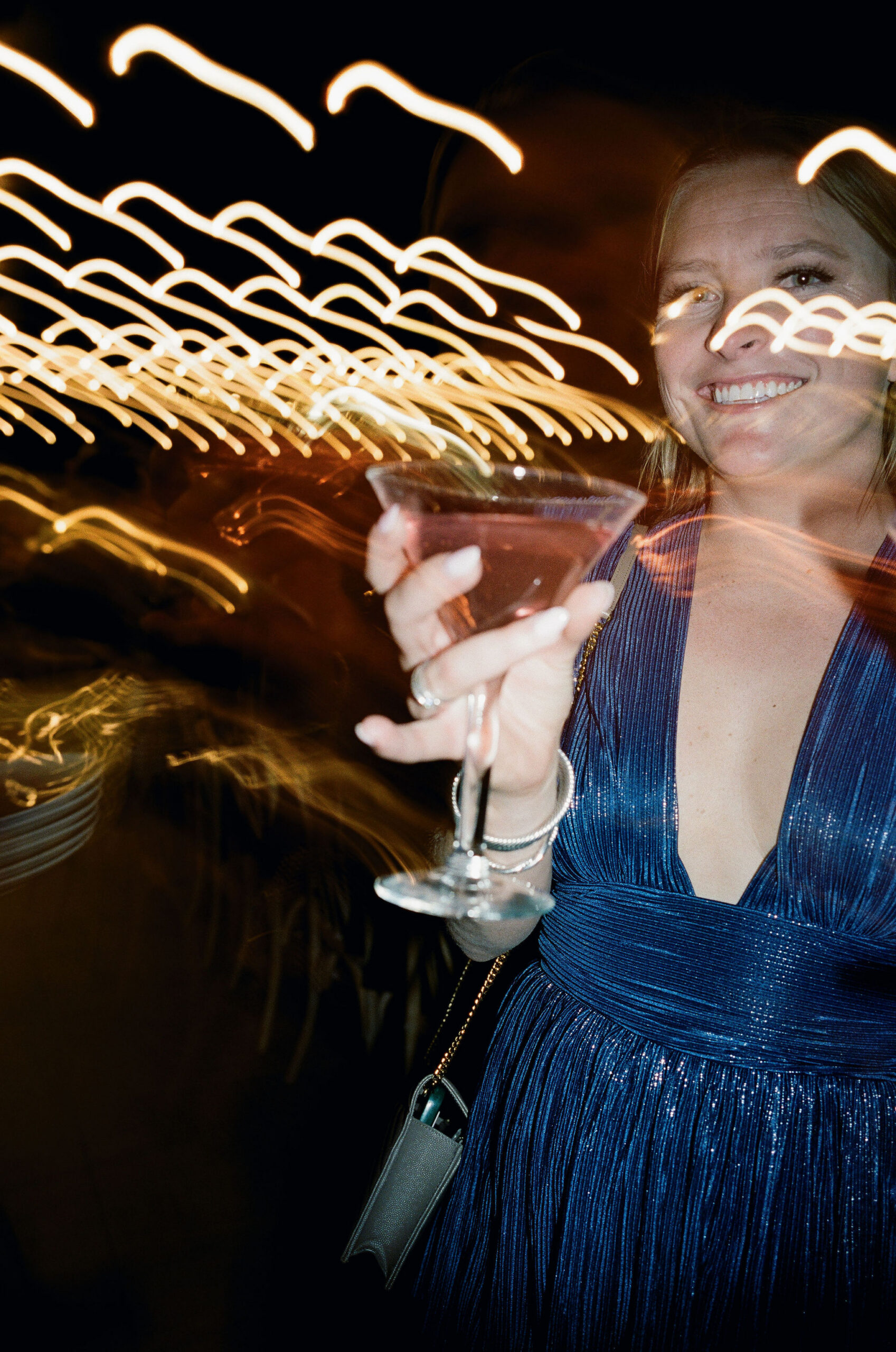 A wedding guest holding a cocktail amid streaks of warm light on film.