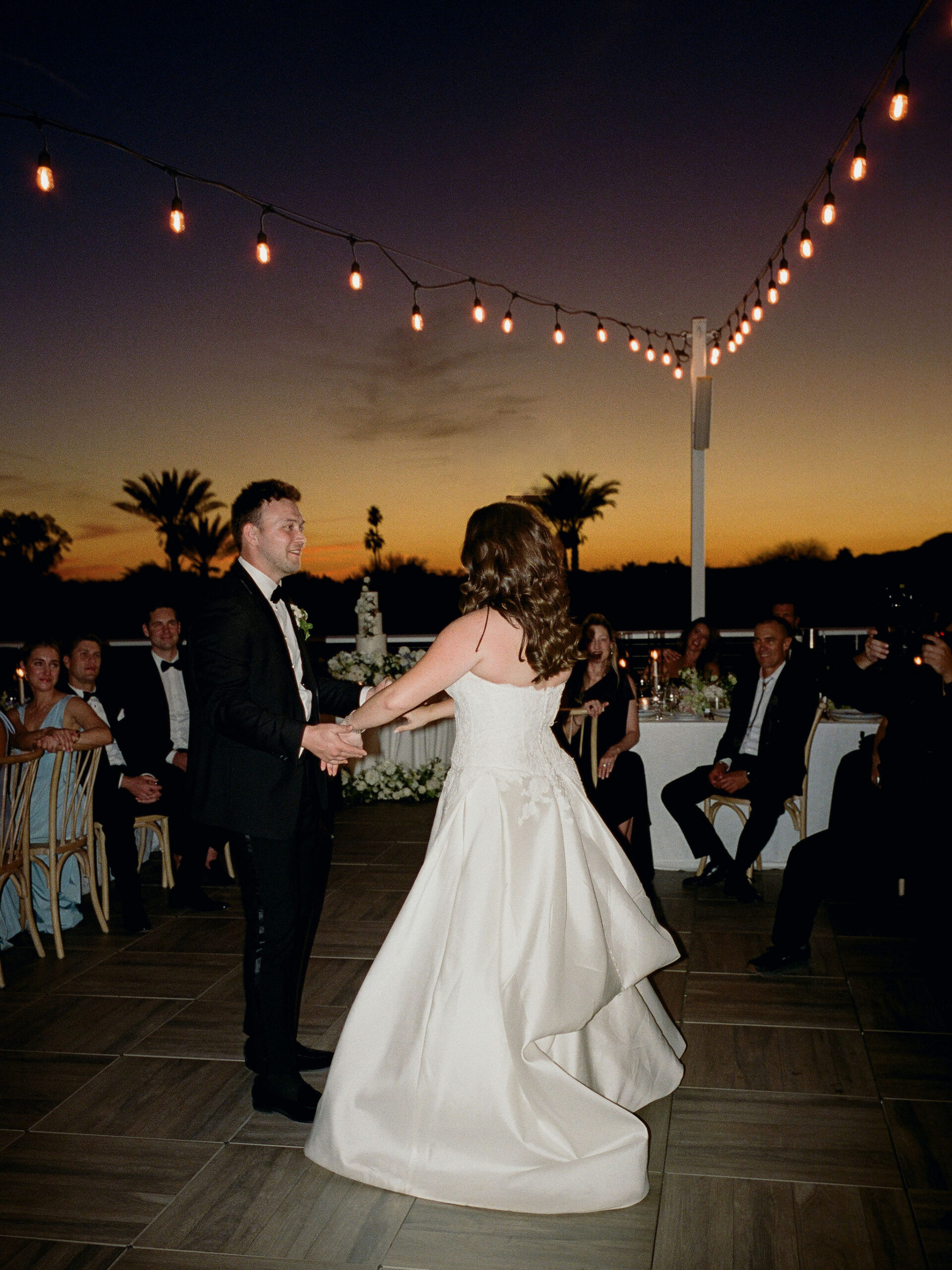 Taylor and Ryan dancing beneath string lights and the sunset on film.