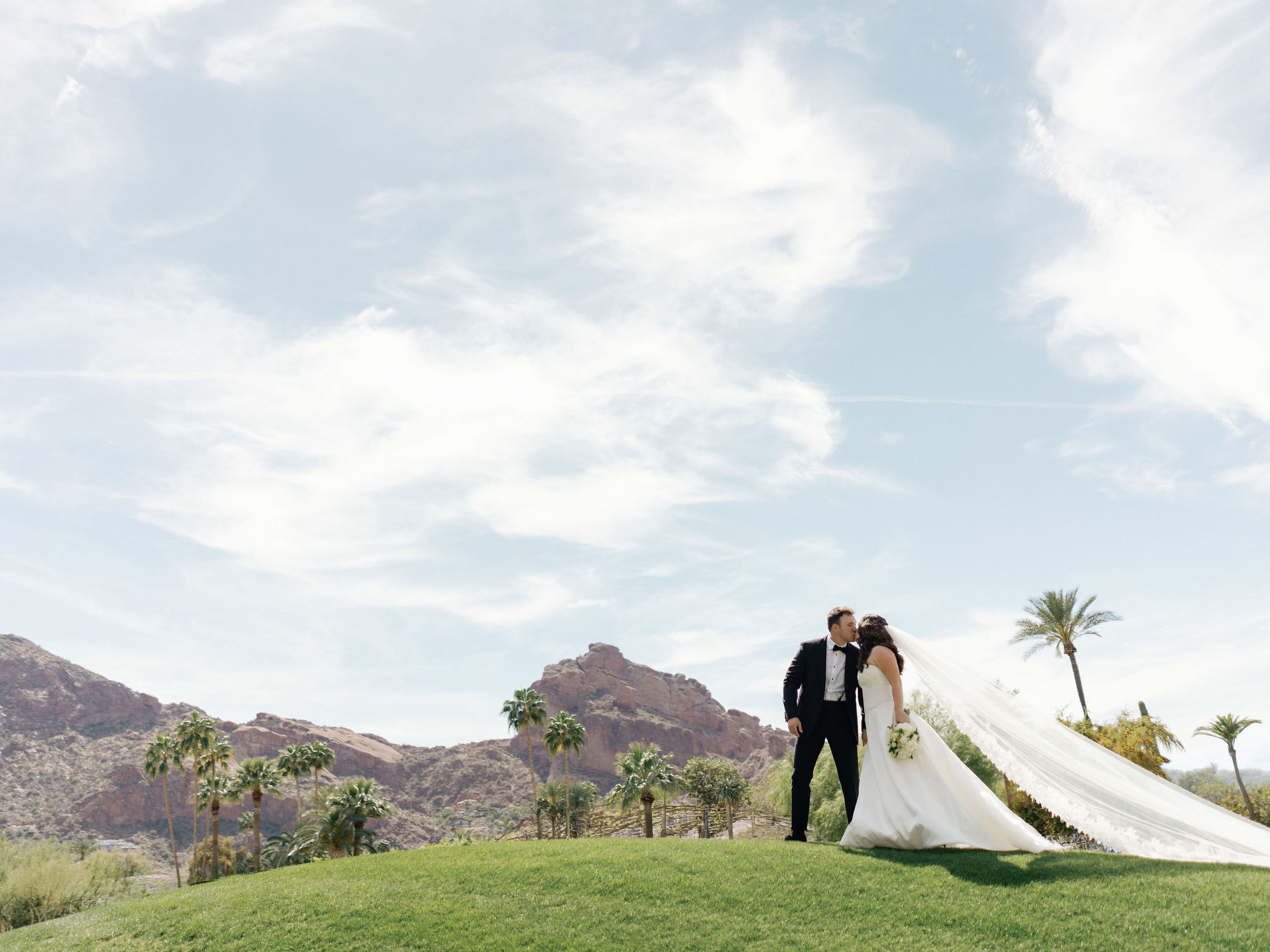 Taylor and Ryan beneath an open sky, with Camelback Mountain and a sweeping veil.