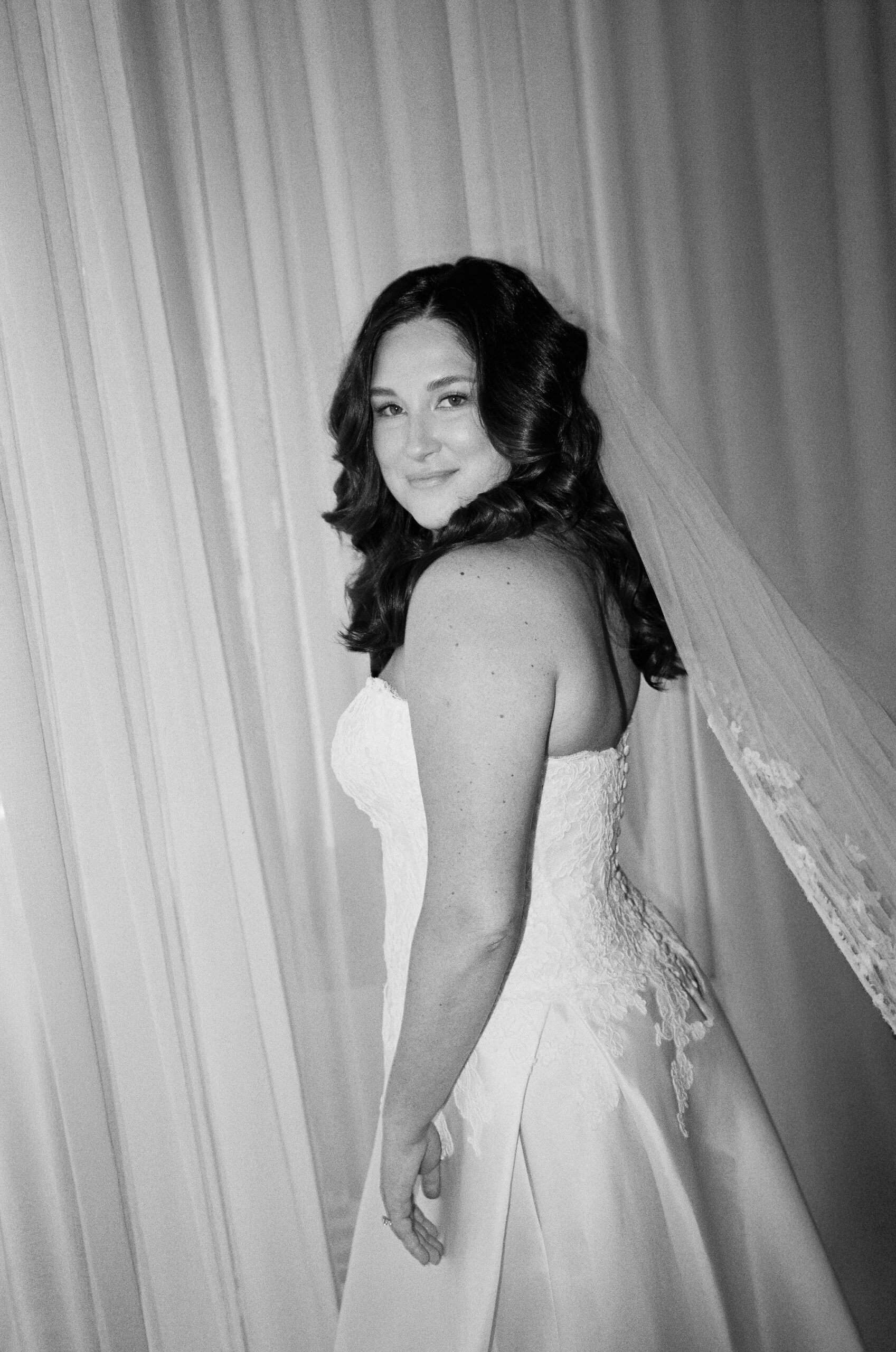 Black-and-white bridal portrait of Taylor beside softly lit curtains.