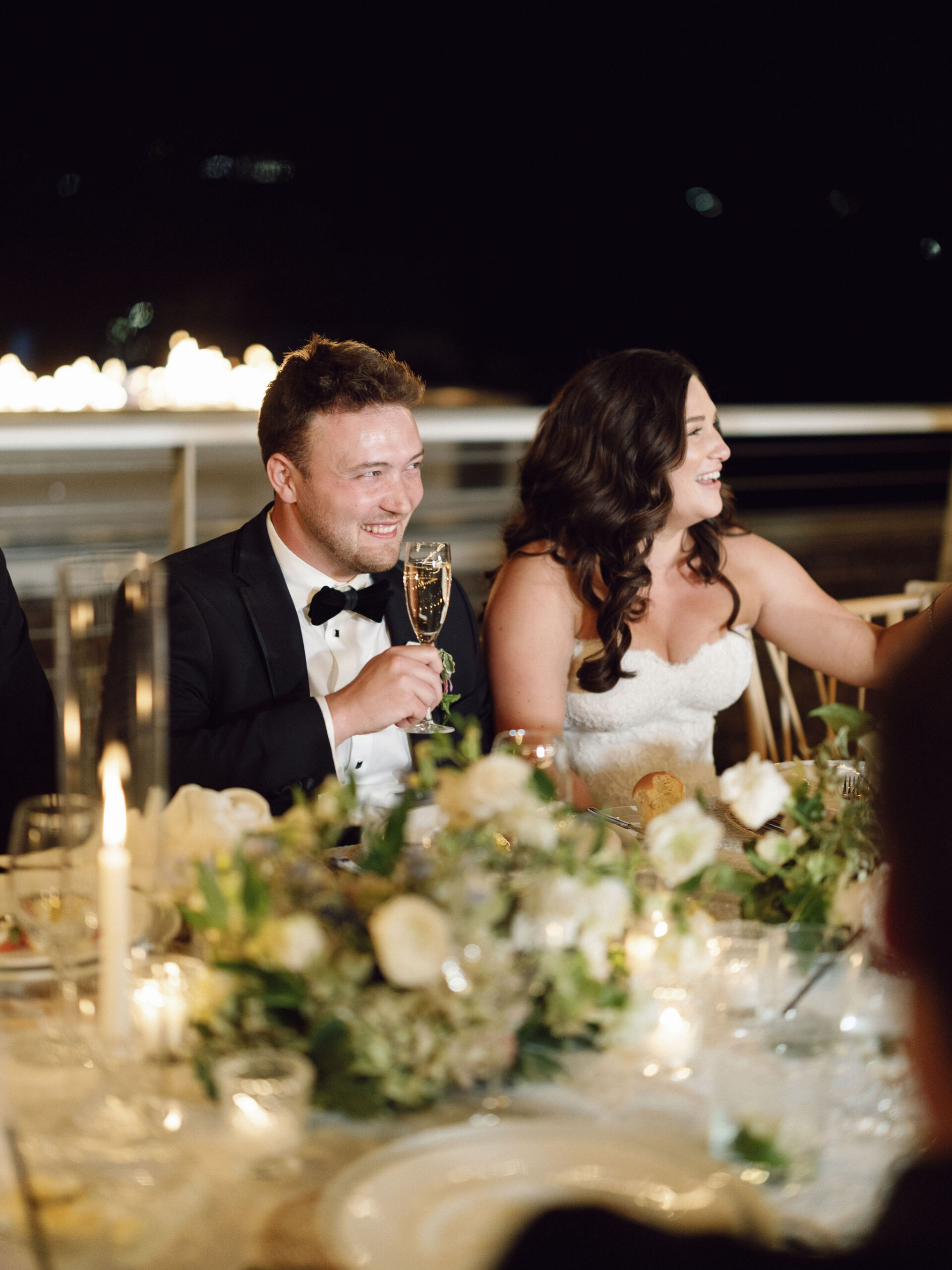 Taylor and Ryan smiling together at their reception table.