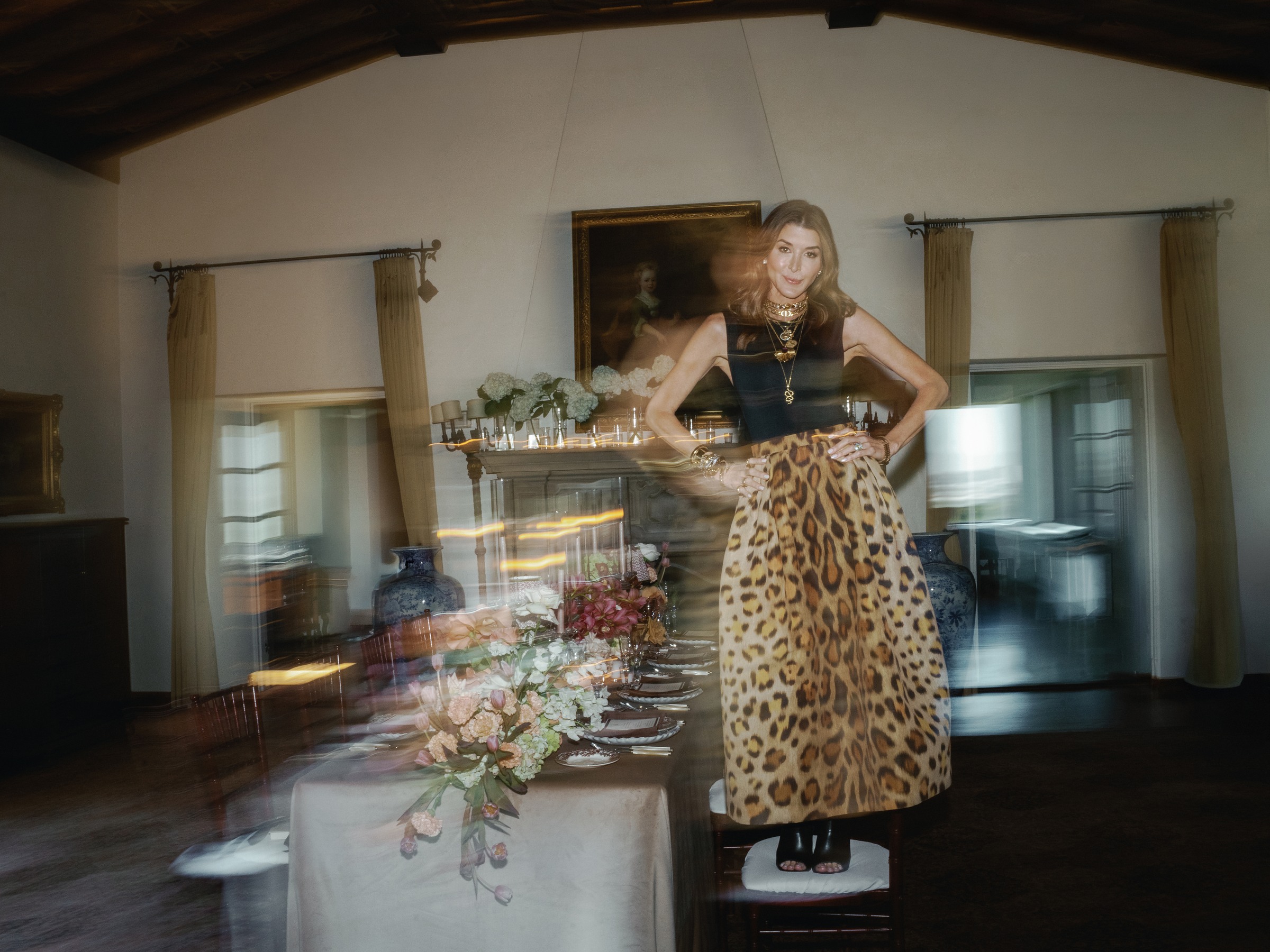 Catherine Tuton in a leopard skirt blurred with motion, standing on a chair in the mansion dining room