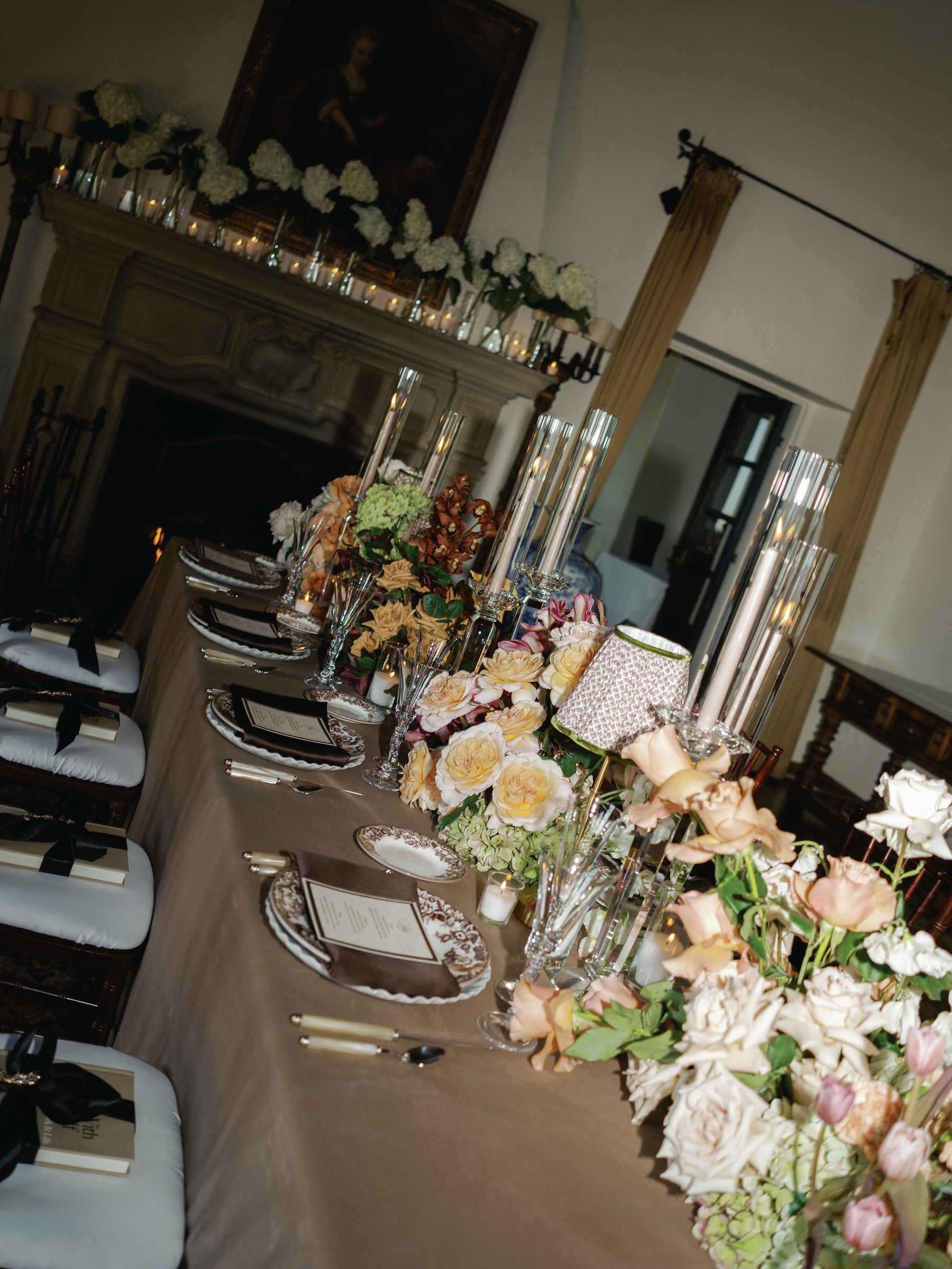 Tilted view down the long dinner table with peach florals and ribbon-tied gift books on each chair
