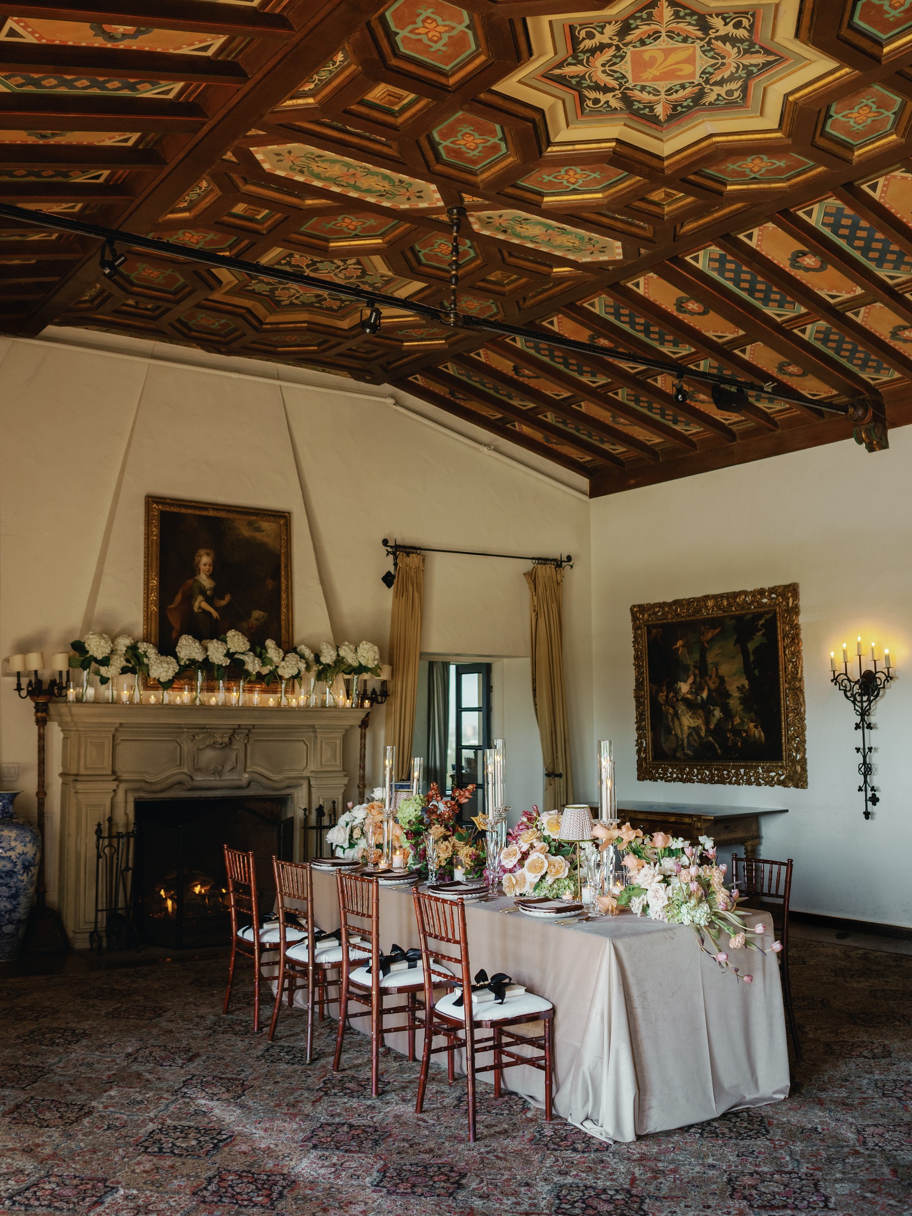 Wrigley Mansion dining room with a painted wood ceiling and a long dinner table set in front of a stone fireplace