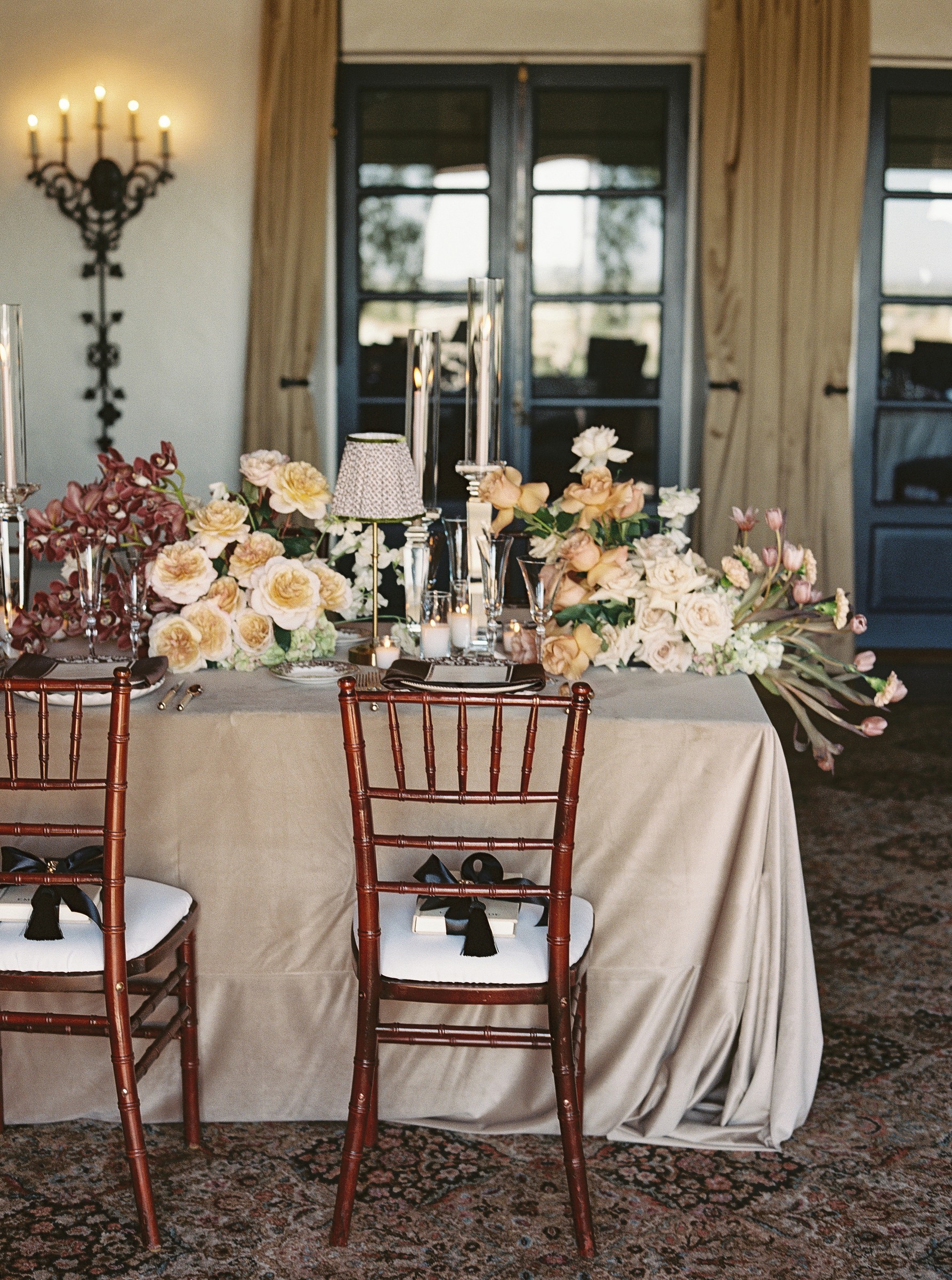 Long dinner table with peach roses and burgundy florals and chiavari chairs tied with black ribbon at the Wrigley Mansion