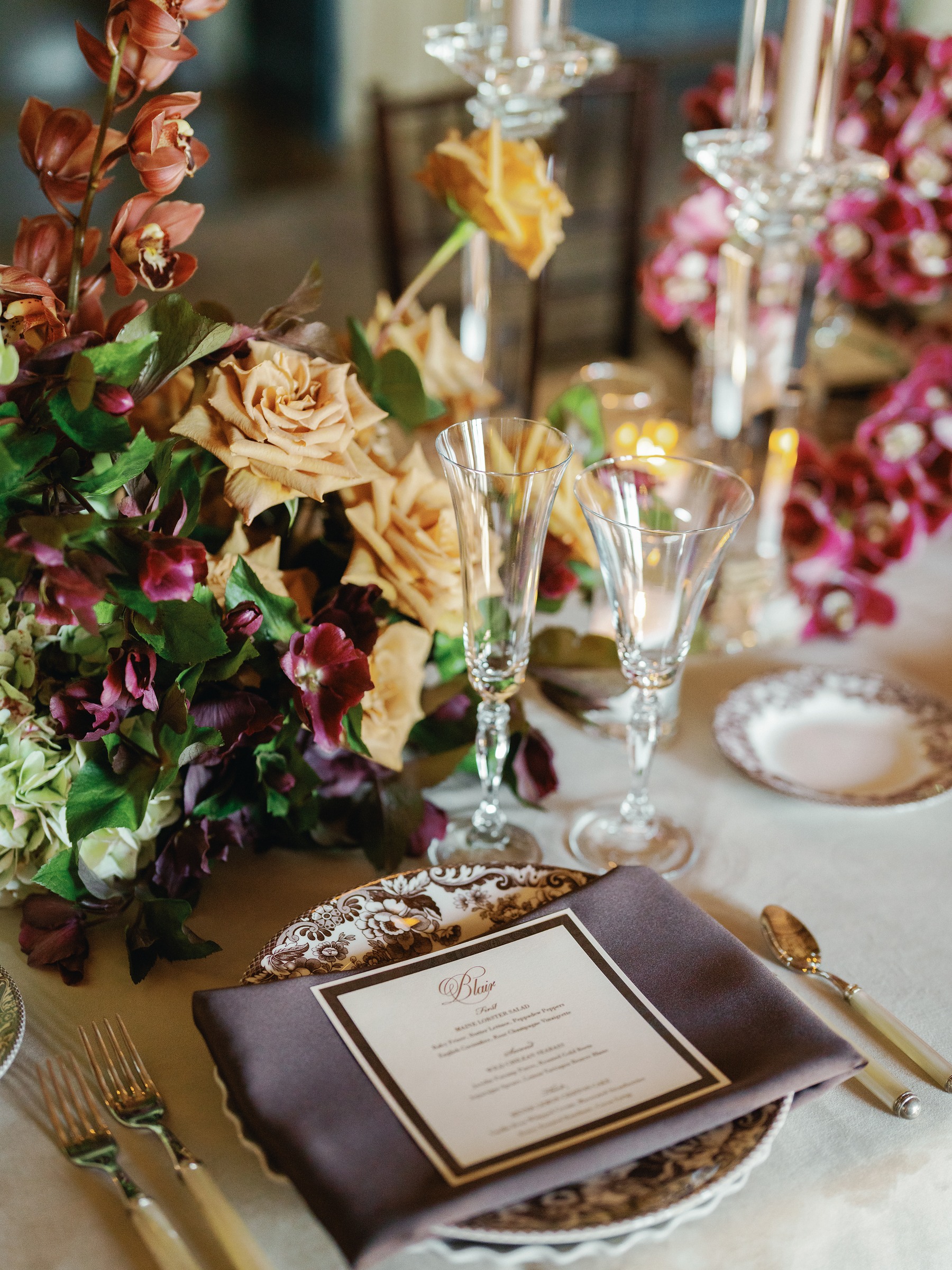 Close-up of burgundy and peach florals beside crystal glasses and a printed menu card
