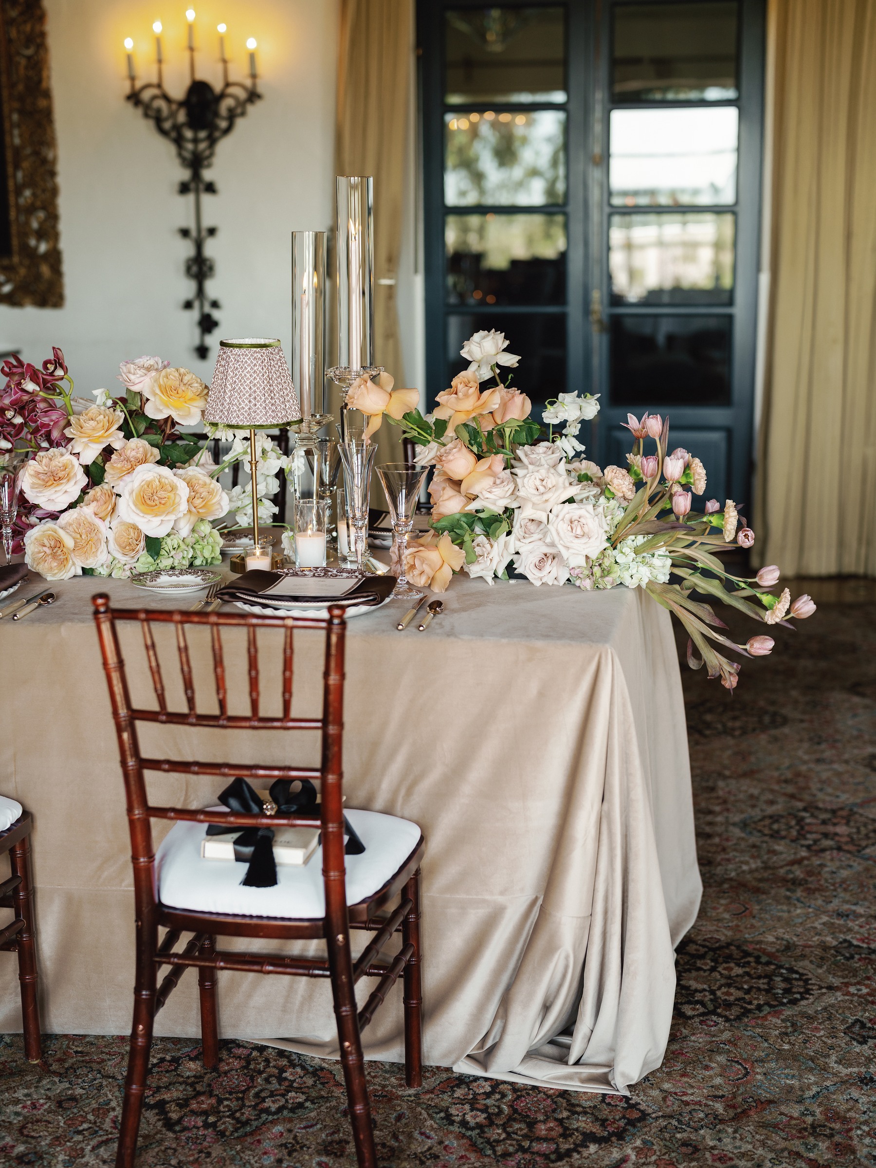 Dinner table by a window with peach florals and a chiavari chair with a black ribbon