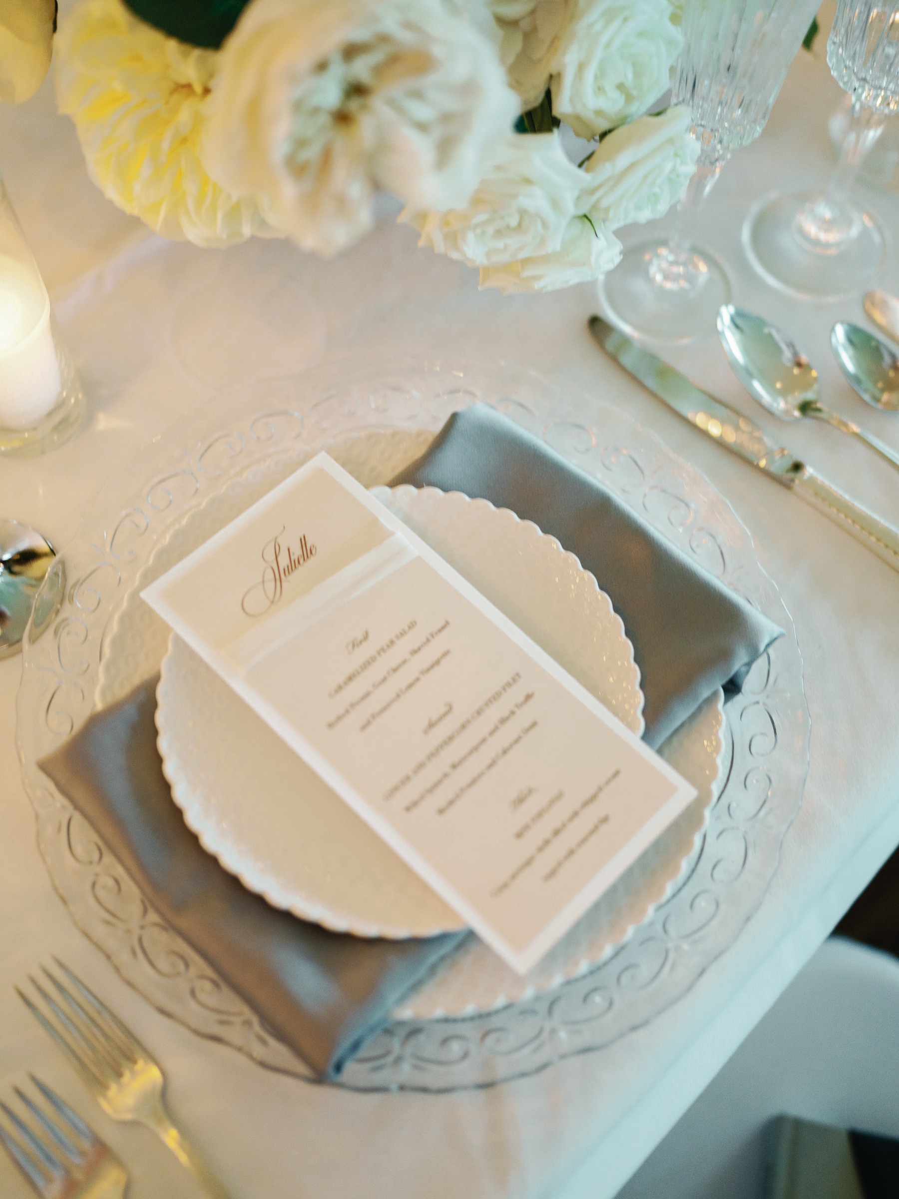Place setting with a gray napkin, scalloped plate, and printed menu on a glass charger