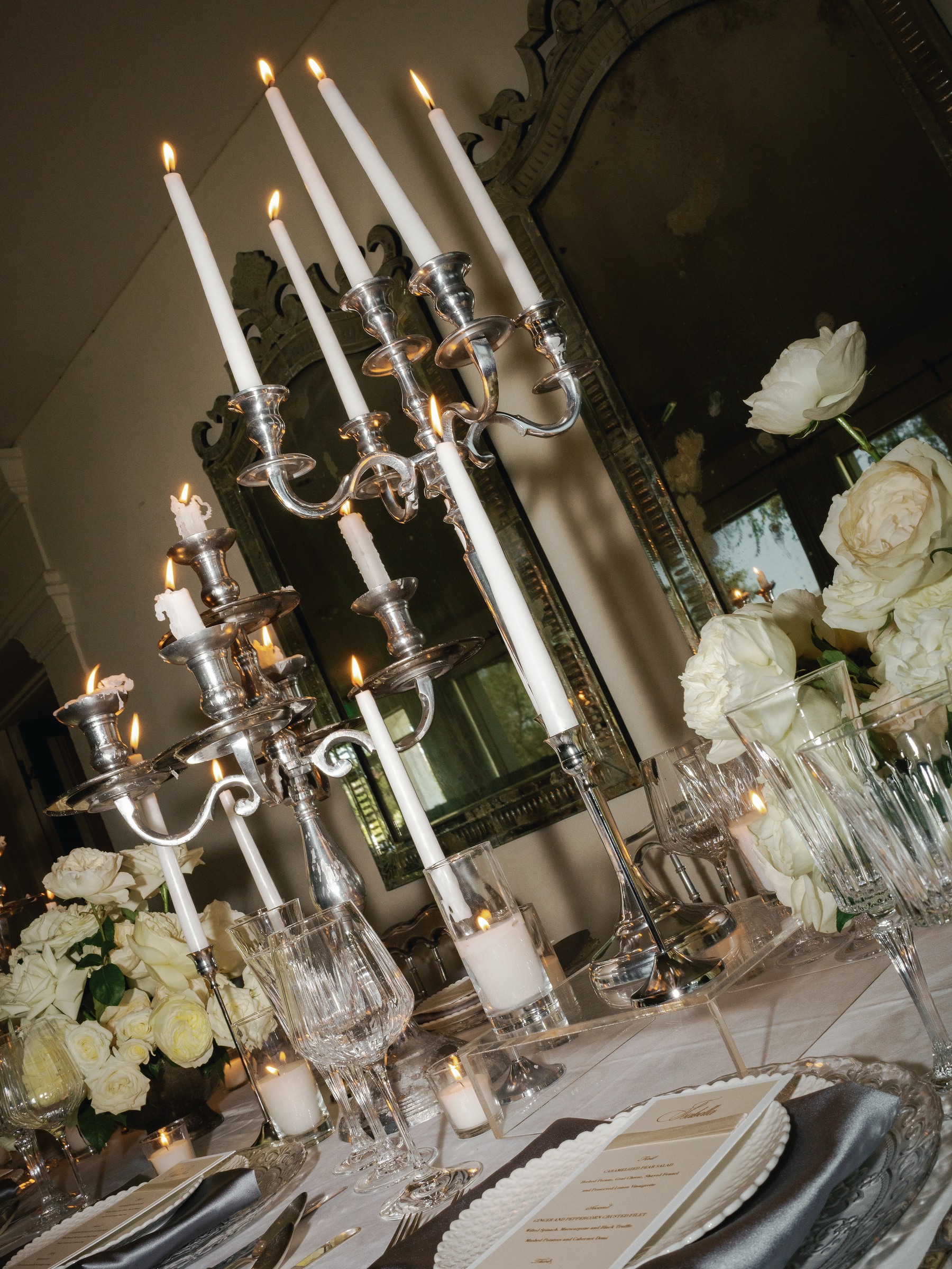 Tilted silver candelabra and white roses over a place setting in the mirrored room