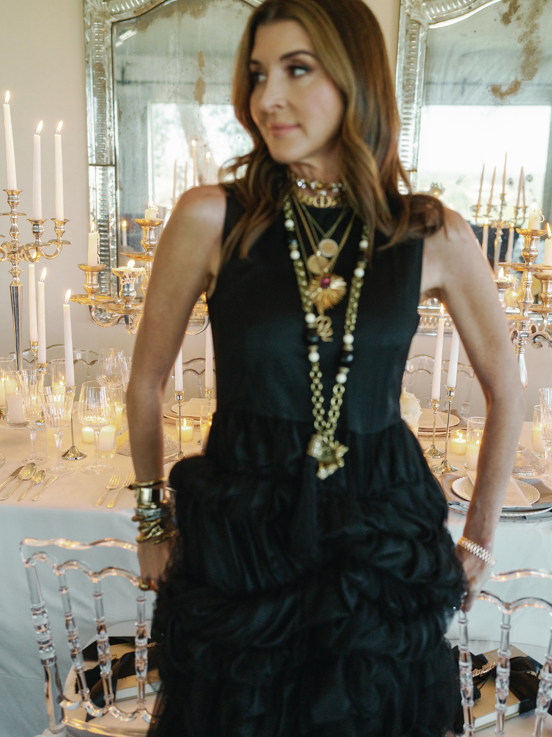 Catherine Tuton in a black ruffled dress with her hands on her hips in front of mirrors and candles